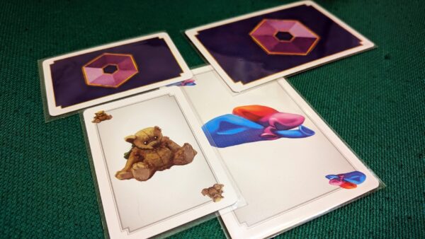 Carte da gioco su un tavolo verde: una con un orsacchiotto, una con forme colorate e due coperte