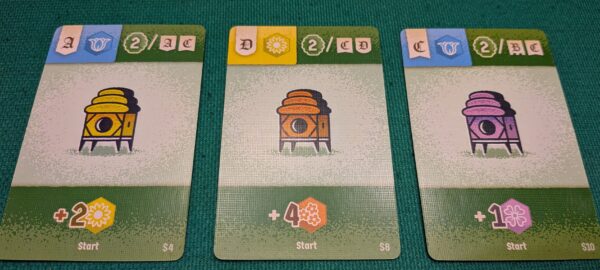 Tre carte da gioco con arnie di colore giallo, arancione e viola, icone di fiori e valori numerici